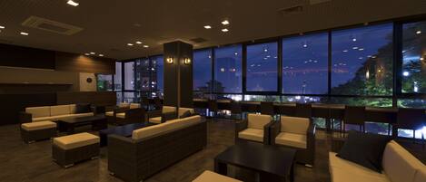 A modern lounge area with sofas, chairs, and tables, large windows offering a city view.