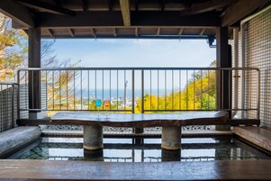 A traditional Japanese onsen with a stone bench and a view of autumn foliage and a cityscape.