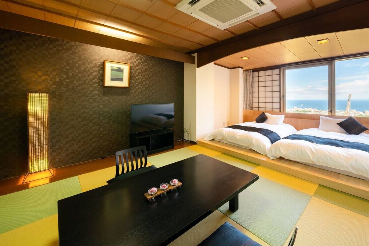 Una habitación con cama, televisor, mesa de comedor y vista al mar.