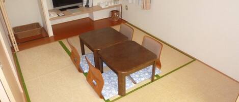 Una habitación pequeña con una mesa y sillas de madera, un televisor y un estante con objetos.