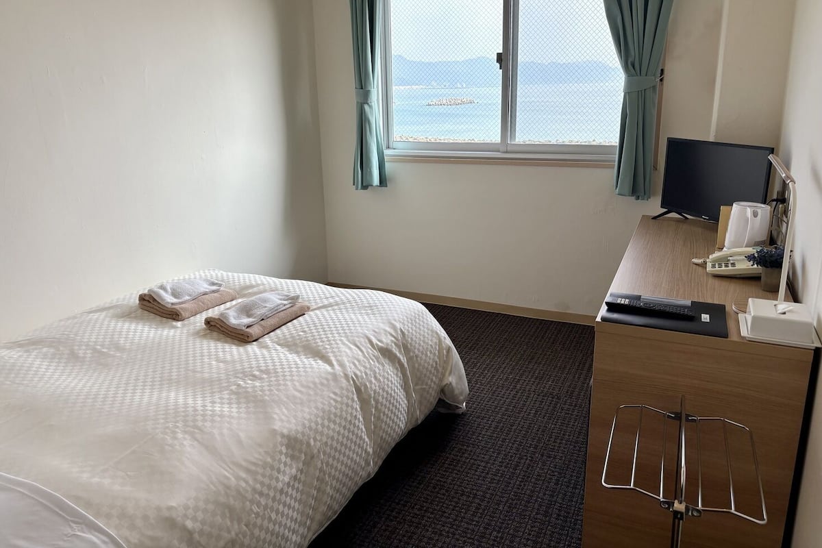 Ein Hotelzimmer mit Bett, Schreibtisch, Computer, Telefon und Fernseher.