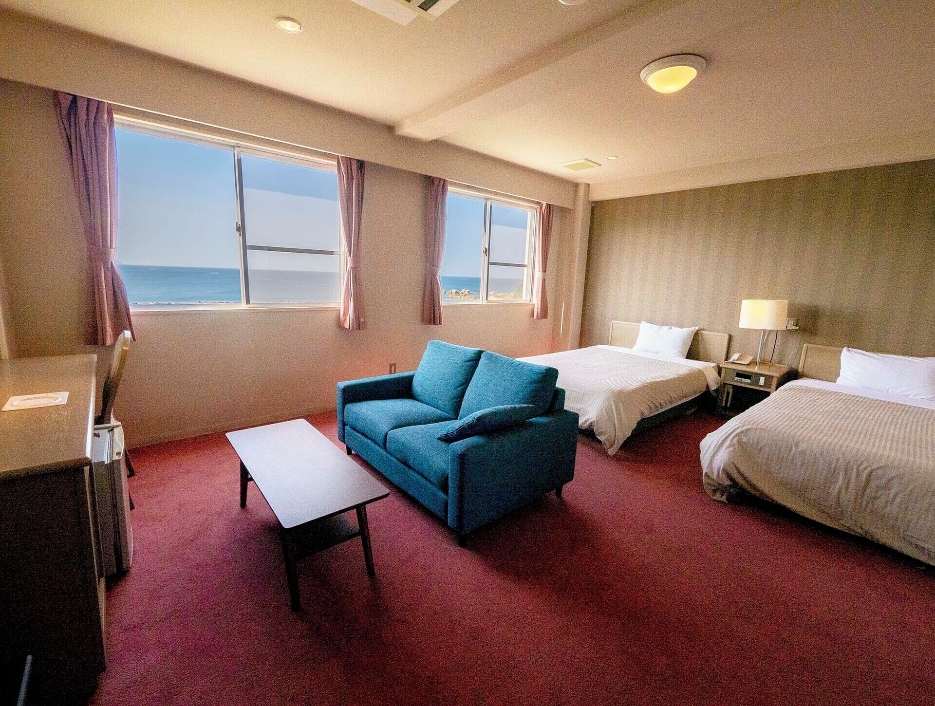 Ein Hotelzimmer mit zwei Betten, einem Sofa, einem Schreibtisch und Meerblick.