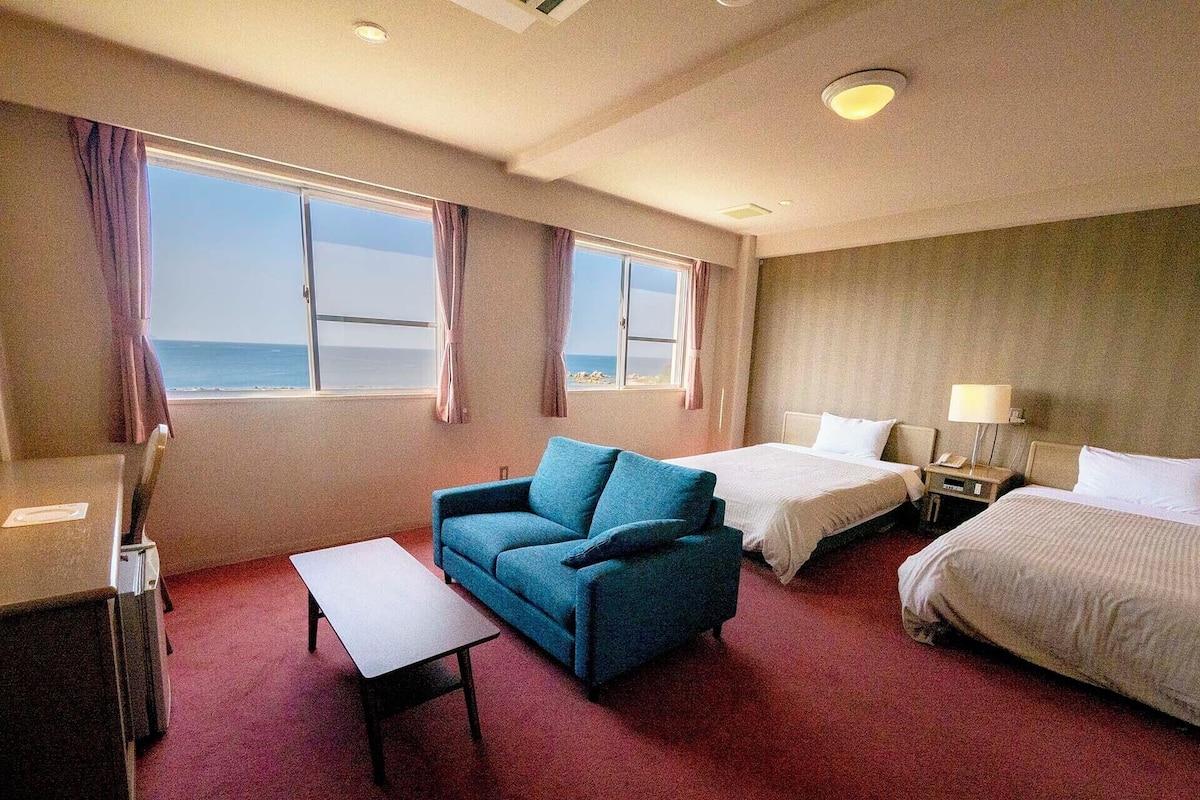 Ein Hotelzimmer mit zwei Betten, einem Sofa, einem Schreibtisch und Meerblick.