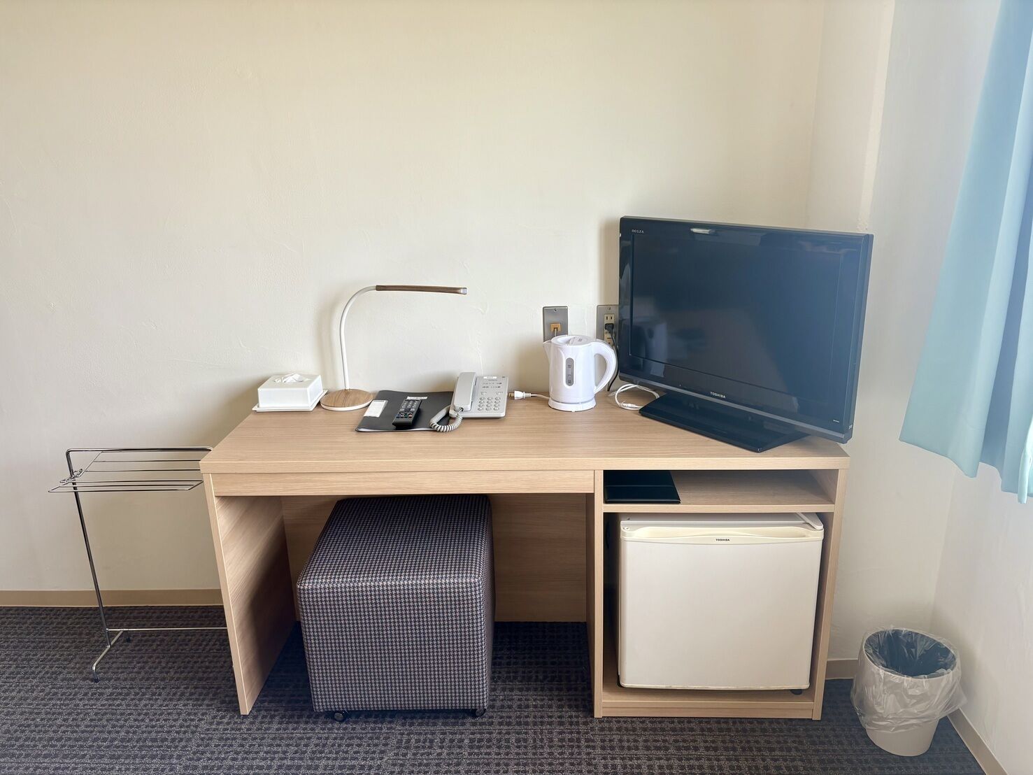 Hotellihuone, jossa on puinen työpöytä, litteänäyttöinen televisio, pöytälamppu, puhelin, kahvinkeitin, pieni jääkaappi ja roskakori.