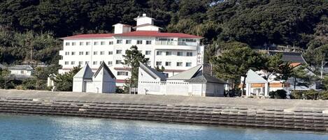 Ein großes Hotel mit mehreren Etagen und einem roten Dach, gelegen am Wasser mit einer Steinfassade im Vordergrund.