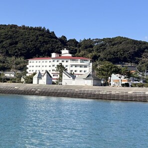 Un grand hôtel à étages, avec un toit rouge, situé au bord de l’eau, devant lequel se trouve une digue en pierre.