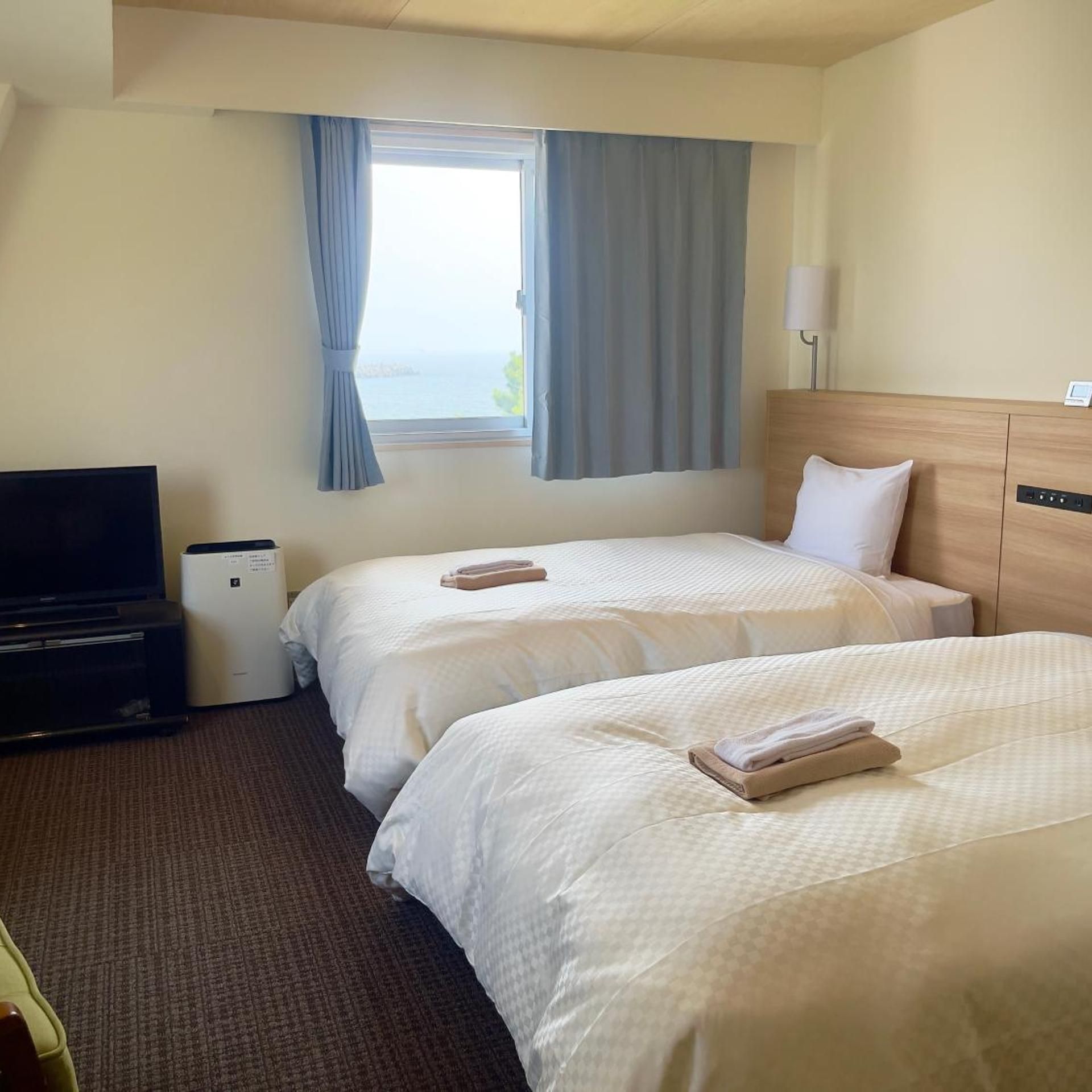 A hotel room with two beds, a TV, a bedside table, and a window with curtains.