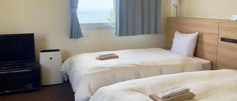A hotel room with two beds, a TV, a bedside table, and a window with curtains.