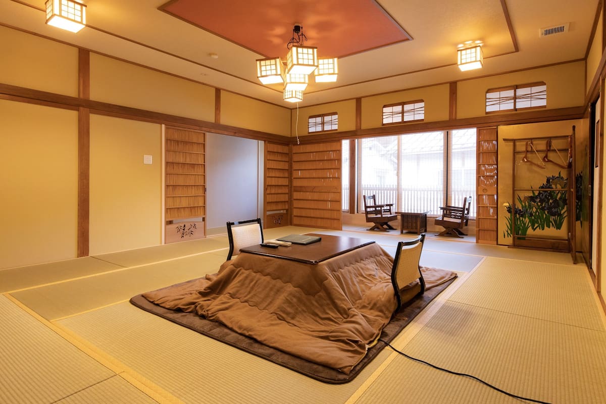 A tatami mat room with a low table, chairs, and a traditional Japanese-style ceiling light.