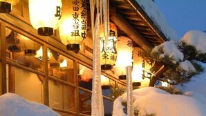 A building with traditional Japanese architecture, surrounded by snow and illuminated by hanging paper lanterns.