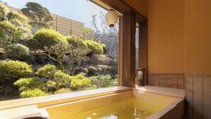 A traditional Japanese bath with a wooden interior, a stone basin, and a view of a landscaped garden.