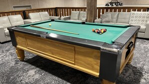 A pool table with a wooden frame and a green felt surface, surrounded by white leather sofas and a wooden bench. - Swagman Chalet (Perisher Valley)