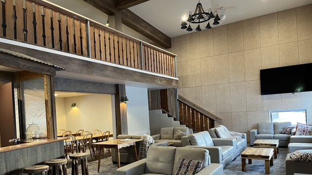 A spacious living area with a high ceiling, a staircase, and a dining area with wooden furniture. - Swagman Chalet (Perisher Valley)