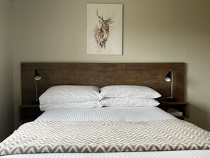 A neatly made bed with a patterned blanket, two bedside lamps, and a framed artwork of a deer on the wall. - Swagman Chalet (Perisher Valley)