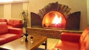 A cozy room with a brick fireplace, red leather sofas, and a small table with glasses. - Swagman Chalet (Perisher Valley)