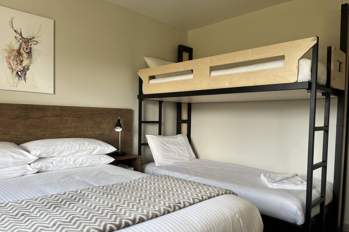 A bunk bed room with a wooden headboard, white bedding, and a wall-mounted lamp.