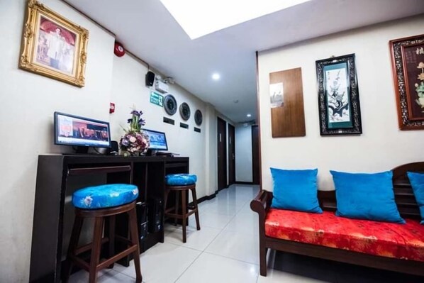 A room with a desk, two bar stools, a sofa with blue cushions, and framed artwork on the walls.