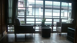 Une pièce dotée d’une grande fenêtre, d’un plancher en bois, d’un canapé, d’un fauteuil et d’une petite table sur laquelle se trouve un vase.