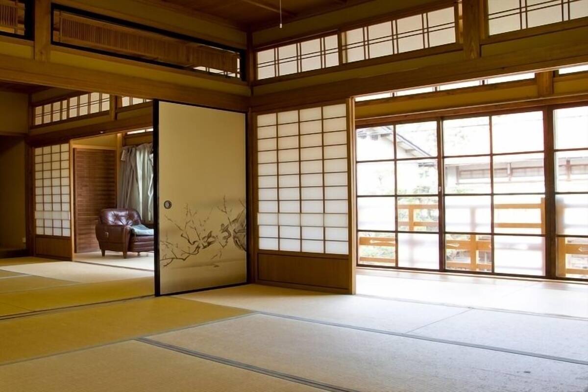 Une pièce de style japonais traditionnel, avec un sol recouvert de tatamis, des portes coulissantes et une vue dégagée grâce à de grandes fenêtres.