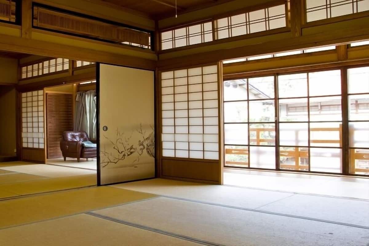 Um quarto japonês tradicional com tatames, portas deslizantes e vista através de grandes janelas.