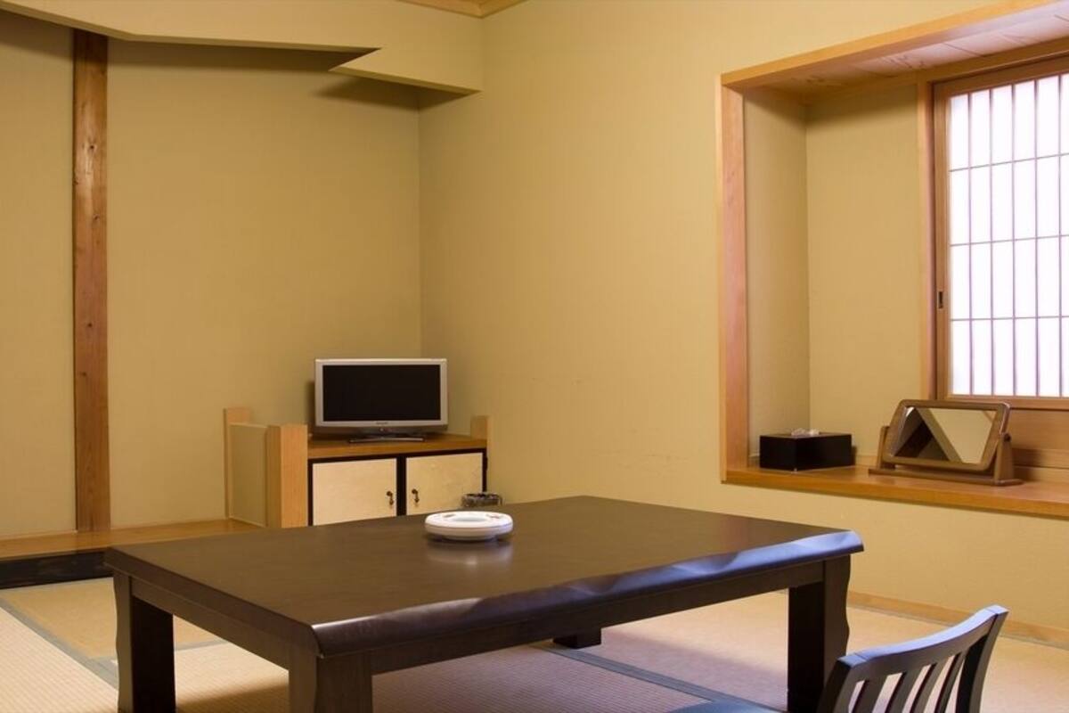 Une pièce de style japonais traditionnel, avec un sol recouvert de tatamis, une table basse, un téléviseur posé sur un meuble et une porte coulissante.