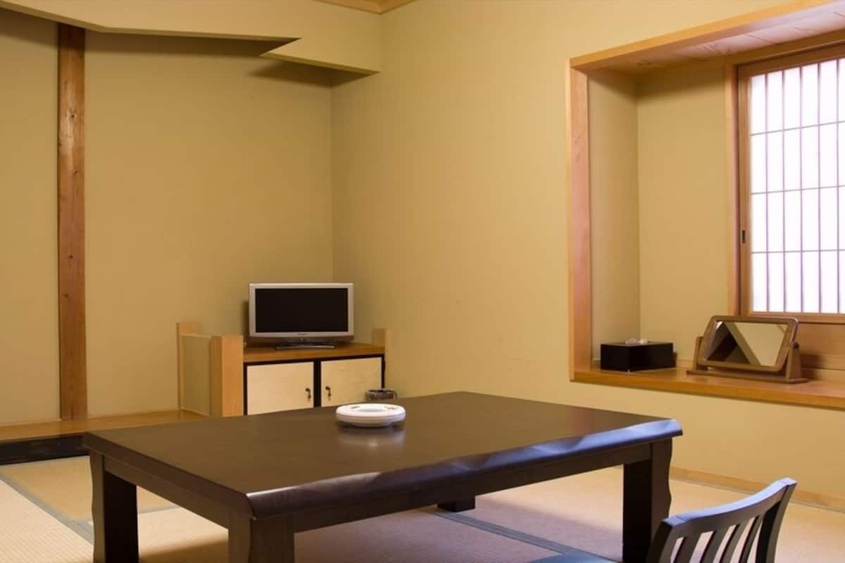 Um quarto japonês tradicional com tatames, uma mesa baixa, uma televisão sobre um móvel e uma porta deslizante.