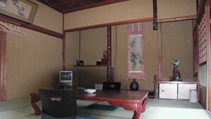 Une pièce de style japonais traditionnel, avec un sol recouvert de tatamis, une table basse, une chaise noire, un téléviseur et un vase décoratif.