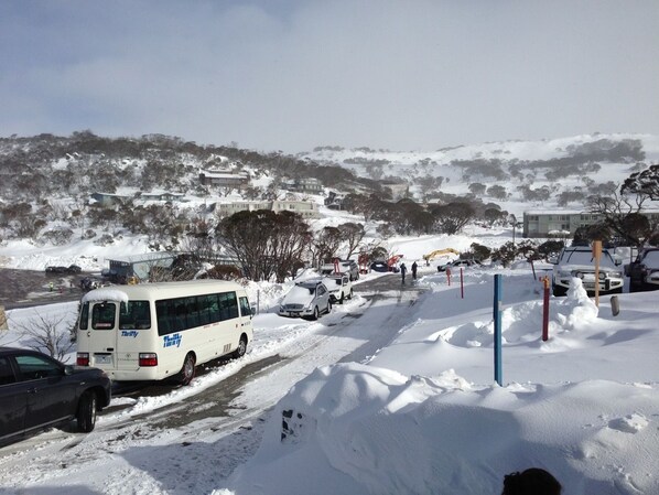 Um estacionamento coberto de neve, com uma carrinha branca e vários carros.