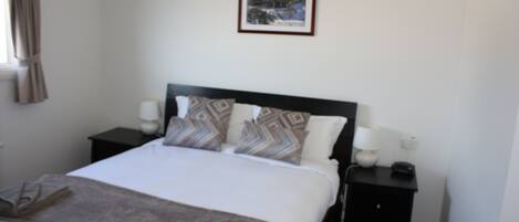 A neatly made bed with patterned pillows, a bedside table with a lamp, and a framed picture on the wall.
