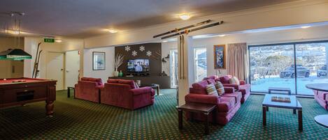 A room with a pool table, red sofas, a television, and a large window with a view of the outside.