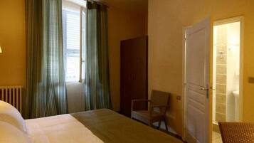 Habitación de hotel con una cama, una silla, un espejo y una puerta que da a un baño.