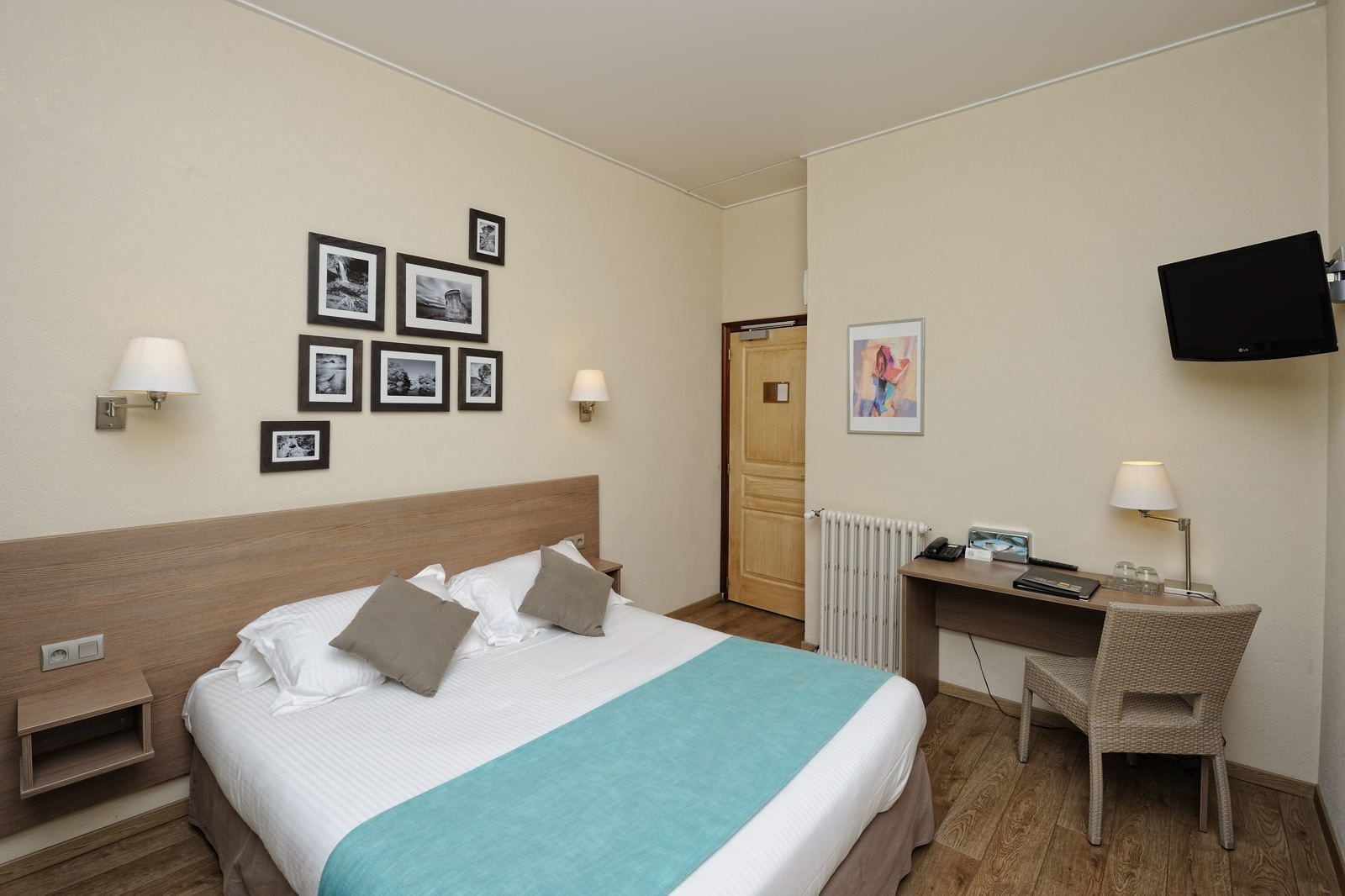 Een hotelkamer met een bed, een bureau, een stoel, een televisie en ingelijste foto's aan de muur.