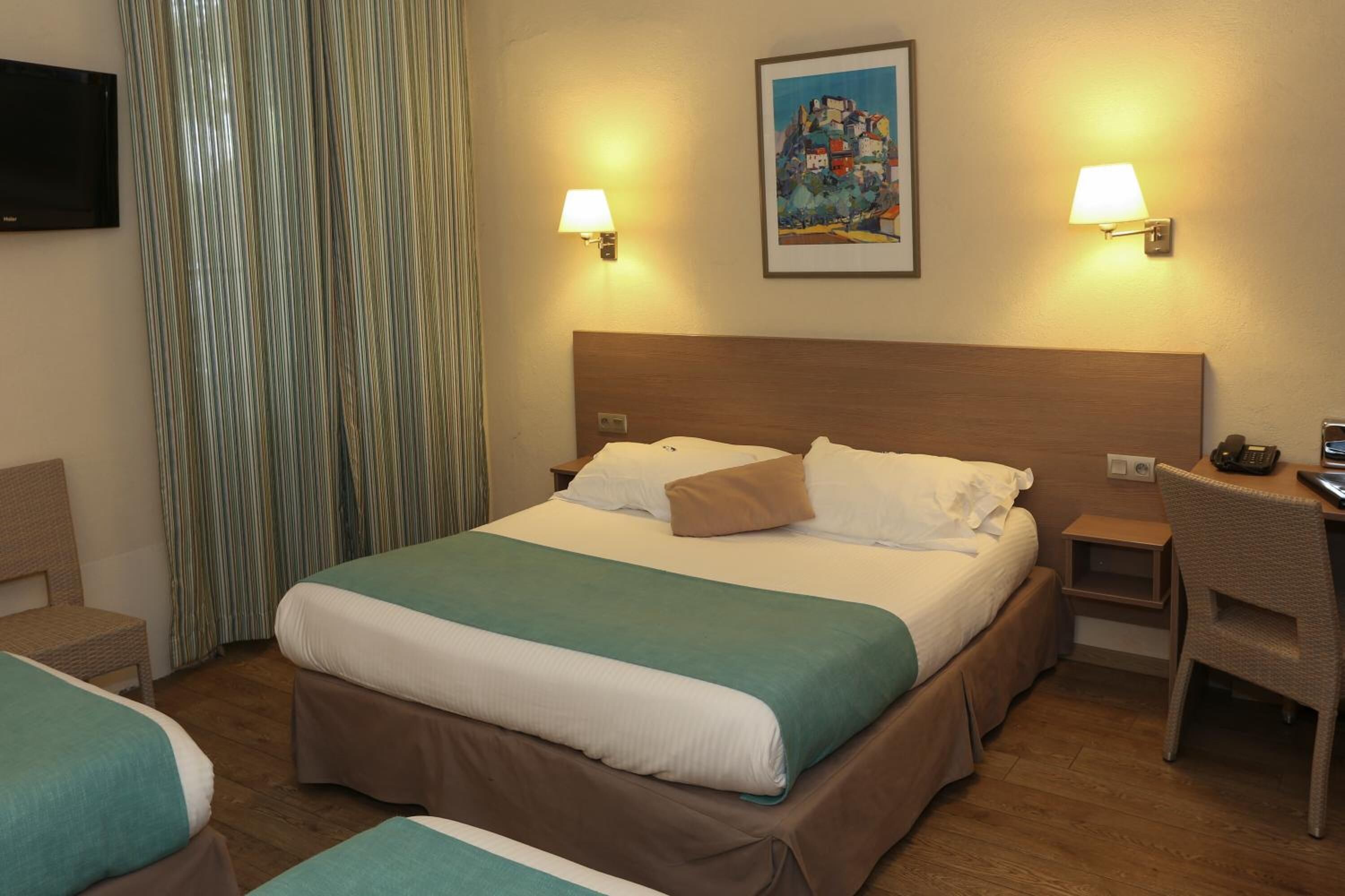 A hotel room with a large bed, two bedside tables, a desk, a chair, and a television.
