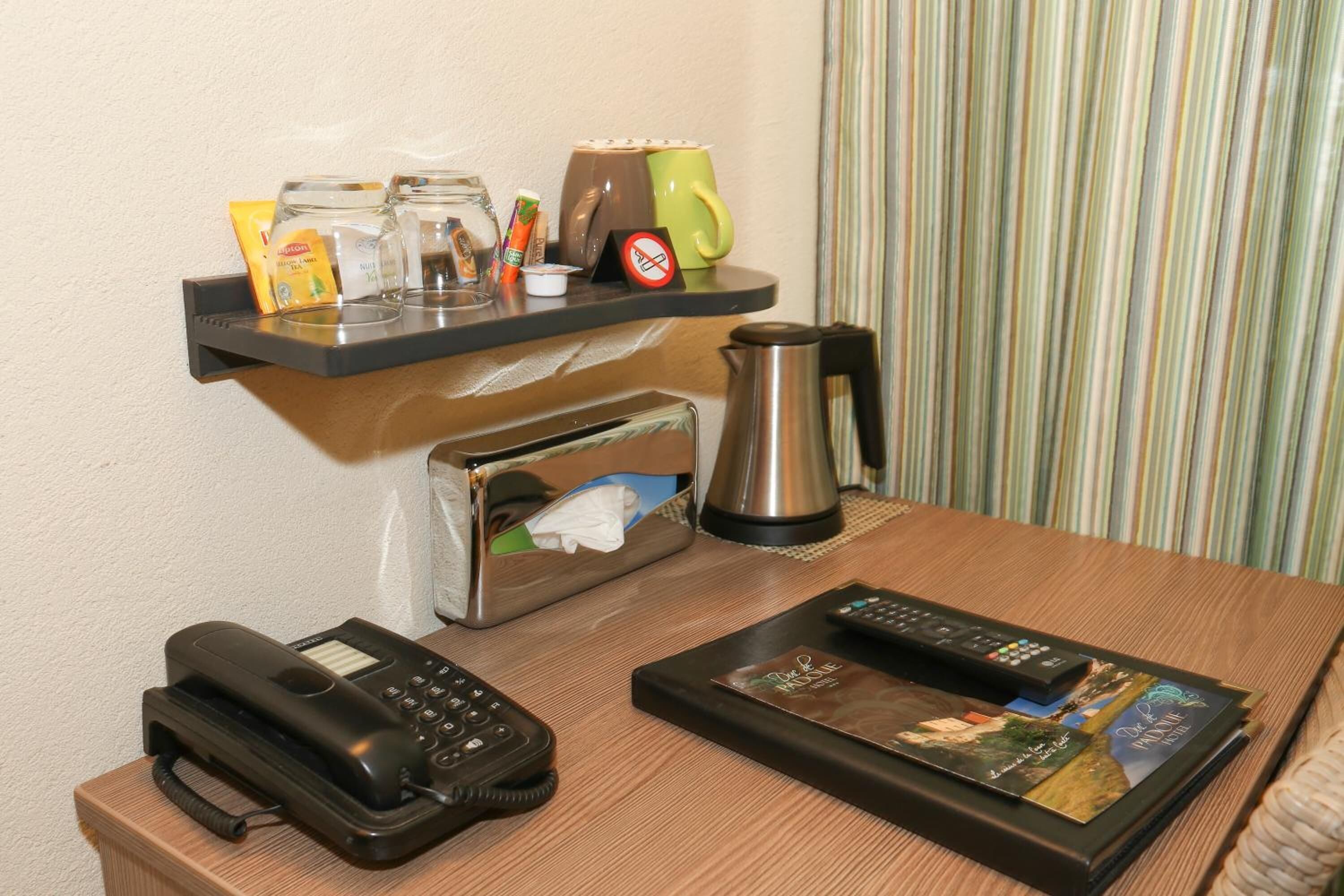 A hotel room with a wooden desk, a telephone, a coffee maker, a remote control, a magazine, and a shelf with toiletries.