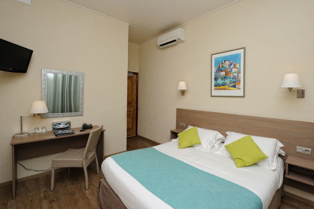 Une chambre d’hôtel avec un lit, un bureau, une chaise, une télévision et un tableau au mur.