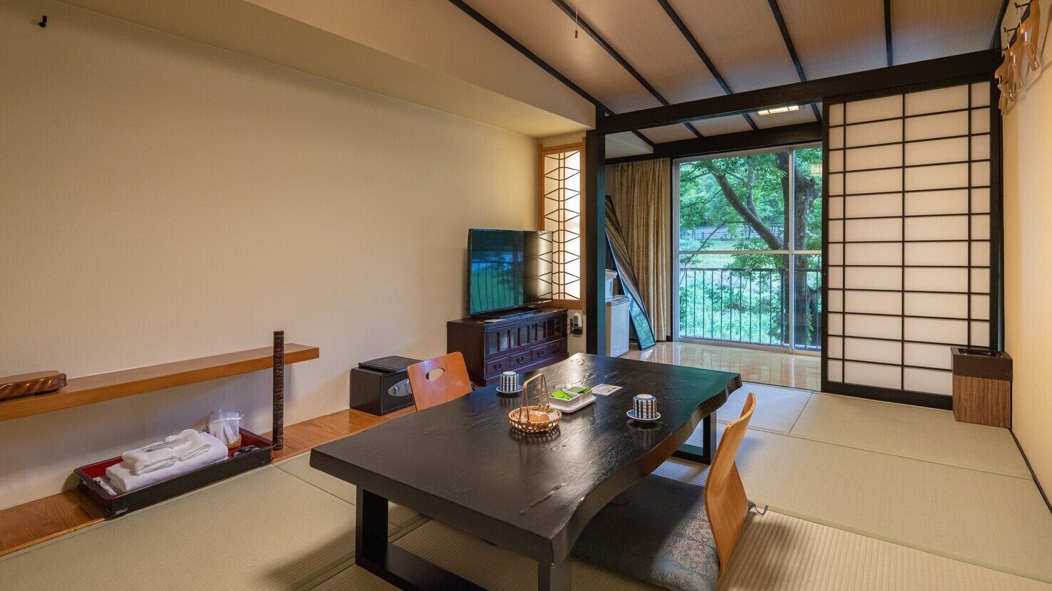 Una habitación tradicional japonesa con suelo de tatami, una mesa baja y un puertas correderas que dan a un jardín.