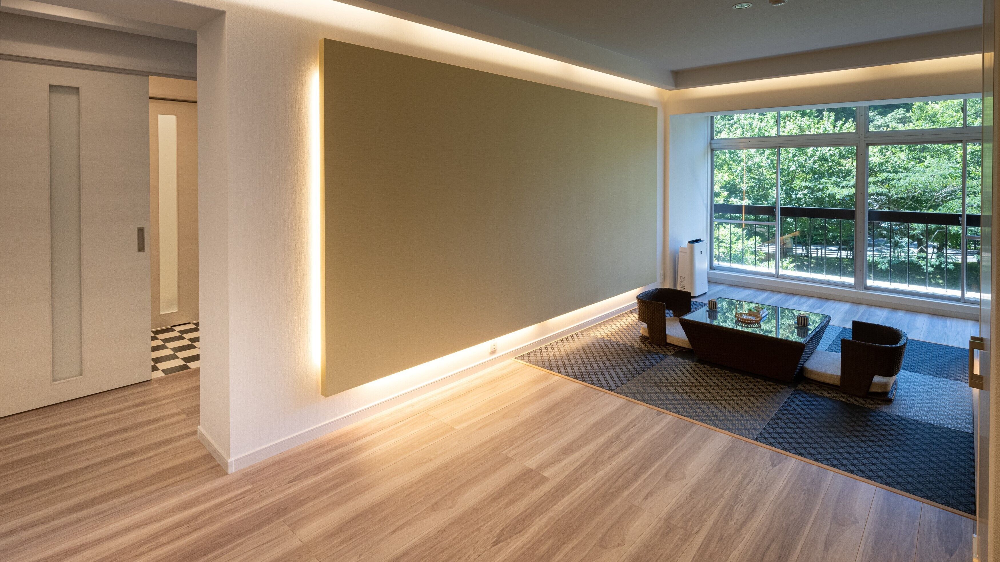 A modern interior with a wooden floor, a glass table, and a view of greenery through large windows.