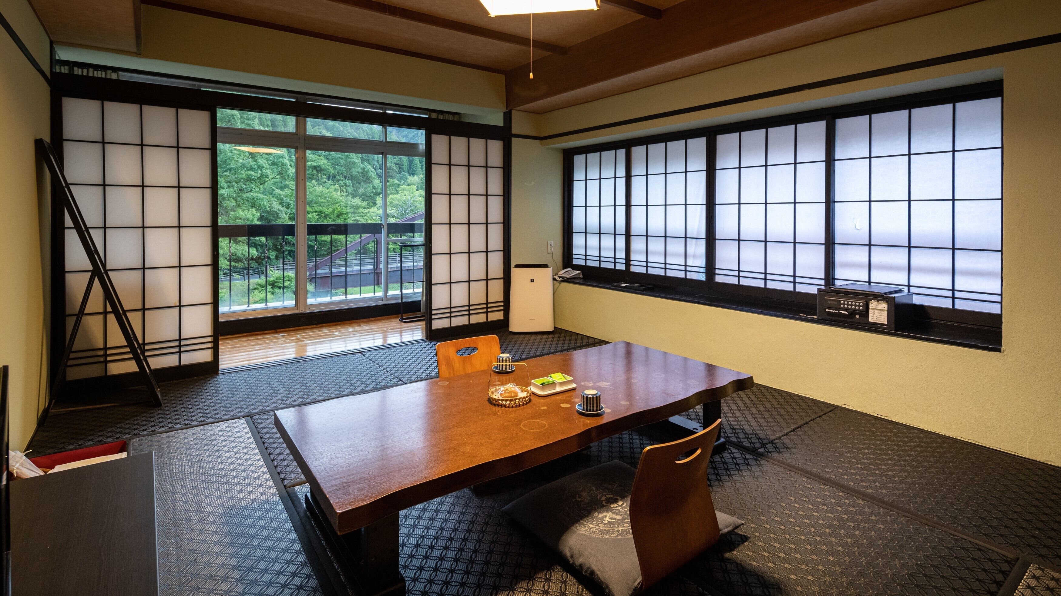 A traditional Japanese room with tatami flooring, a low table, and sliding doors with a view of greenery.