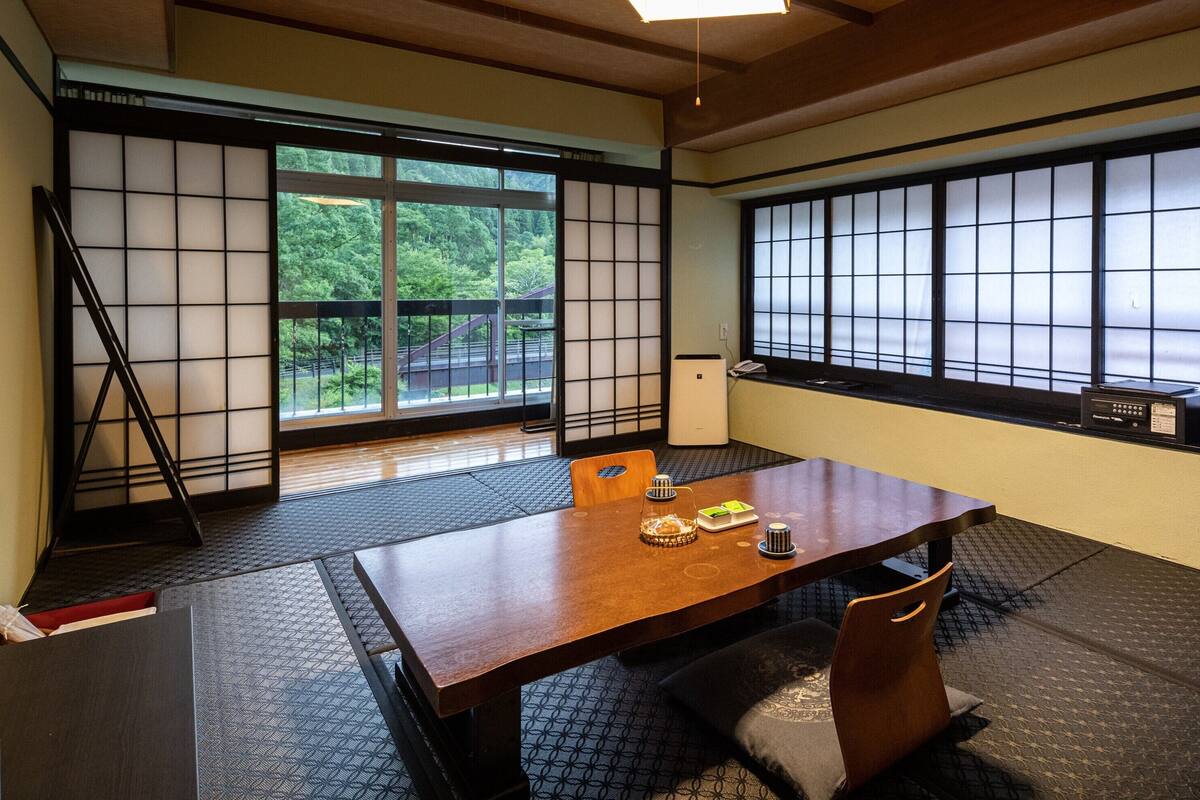 A traditional Japanese room with tatami flooring, a low table, and sliding doors with a view of greenery.