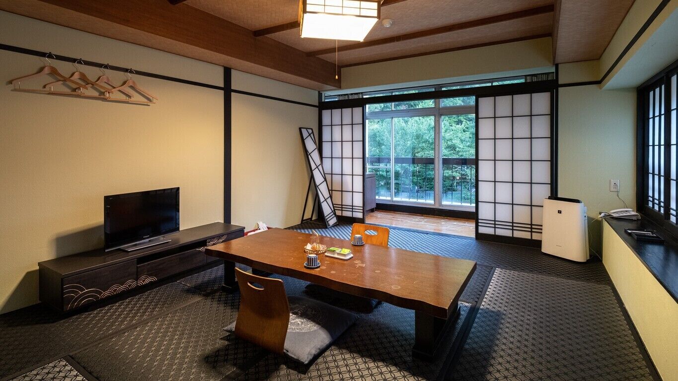 Una habitación de estilo japonés tradicional, con suelo de tatami, una mesa baja, un televisor y puertas correderas.