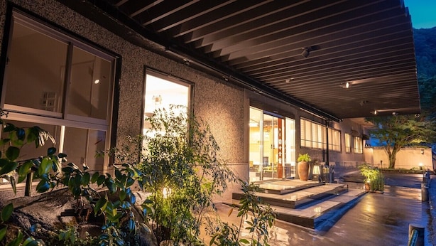 A modern building with large windows, a covered outdoor area, and a water feature. - Tanaka Kaikan (Kirishima)