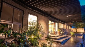 A modern building with large windows, a covered outdoor area, and a water feature. - Tanaka Kaikan (Kirishima)