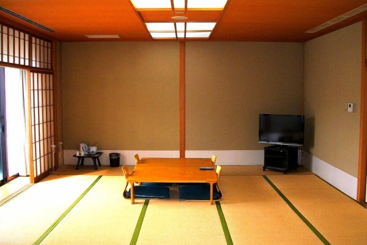 Een traditionele Japanse kamer met tatami vloeren, een laag tatami tafel, een televisie en schuifdeuren.