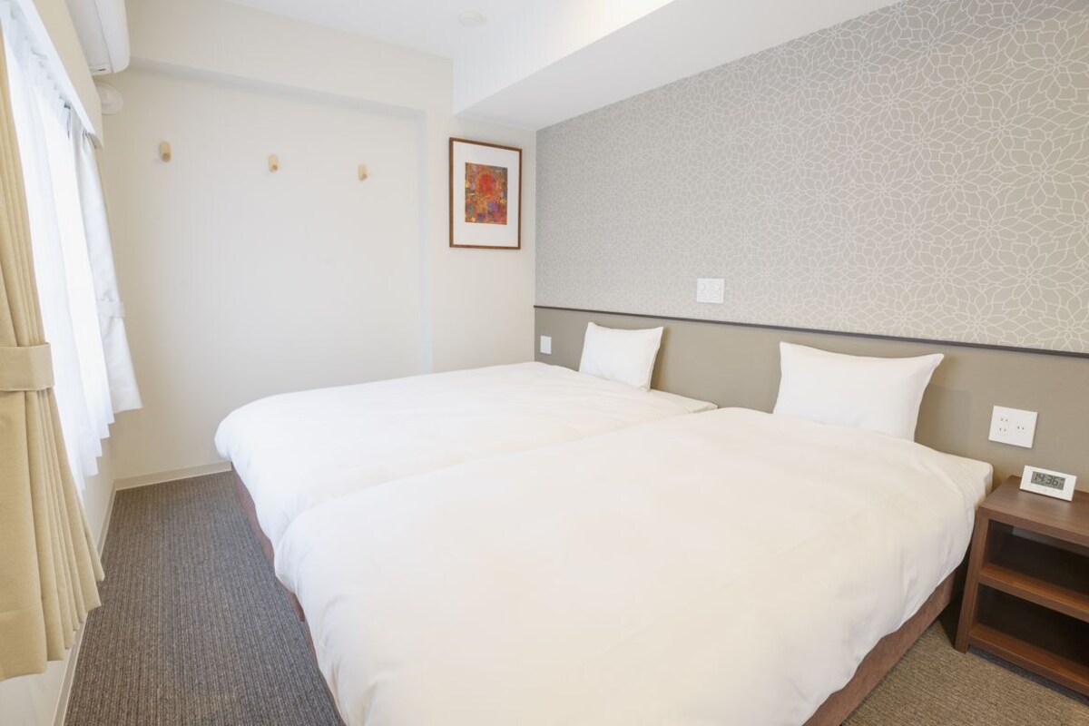 Een hotelkamer met twee bedden, een neutraal kleurenpalet, een gestreept behang en een klein schilderij aan de muur.