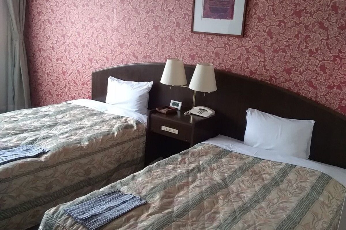 Een hotelkamer met twee bedden, een nachtkastje met lampen, een klok en een ingelijst schilderij aan de muur.