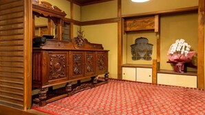A traditional Japanese-style room with tatami flooring, a wooden dresser with carvings, a mirror, and a framed portrait on the wall. - Hotel Amabile Maizuru (Maizuru)