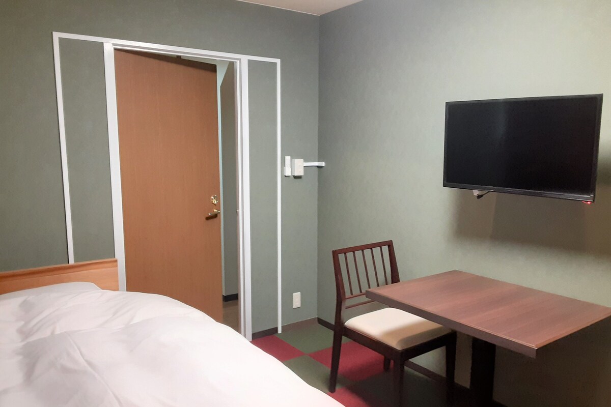 Een hotelkamer met een bed, een houten bureau, een televisie en een deur.