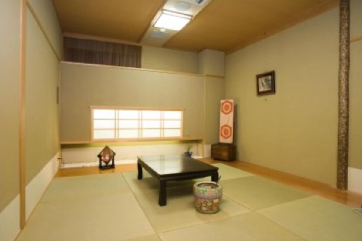 Een traditionele Japanse kamer met tatami vloeren, een lage tafel, een lantaarn en een decoratief object aan de muur.