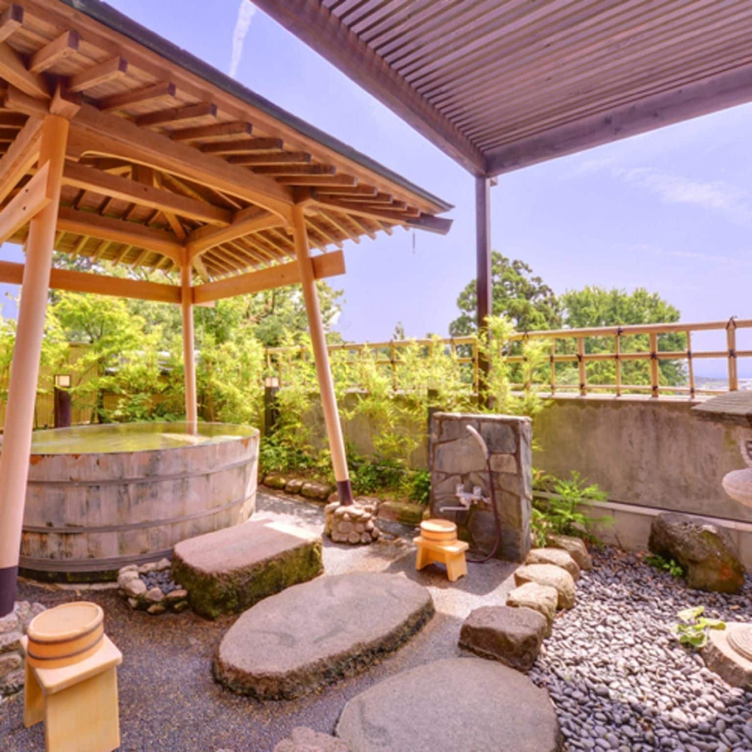 A traditional Japanese outdoor bath area with a wooden pavilion, stone steps, and a stone water feature.