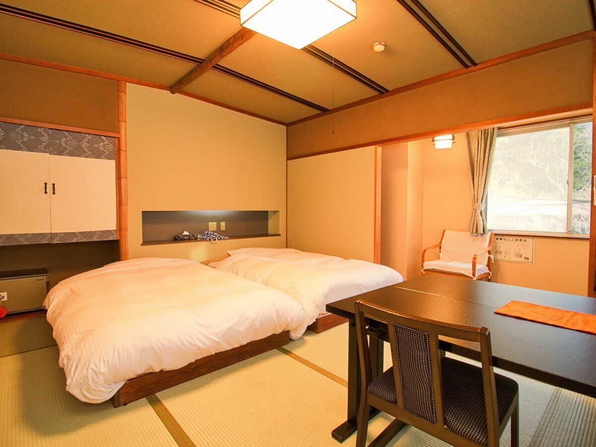 A hotel room with two beds, a small table, and a window with curtains.